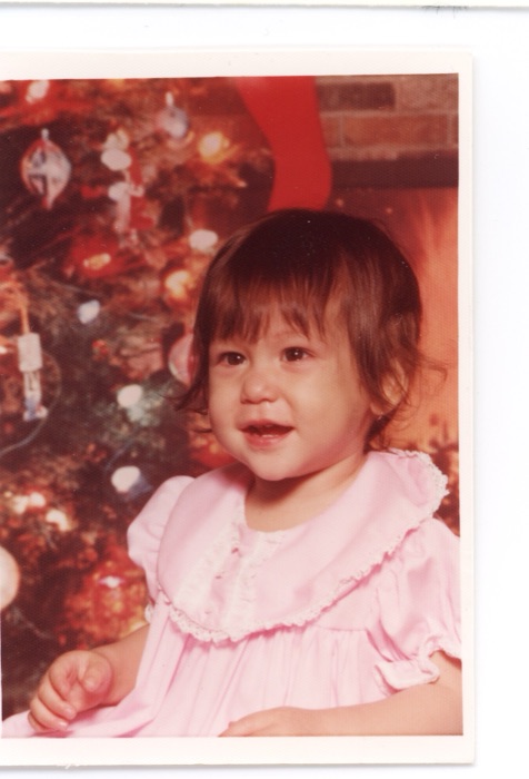 Amanda as a toddler, in front of a Christmas tree.
